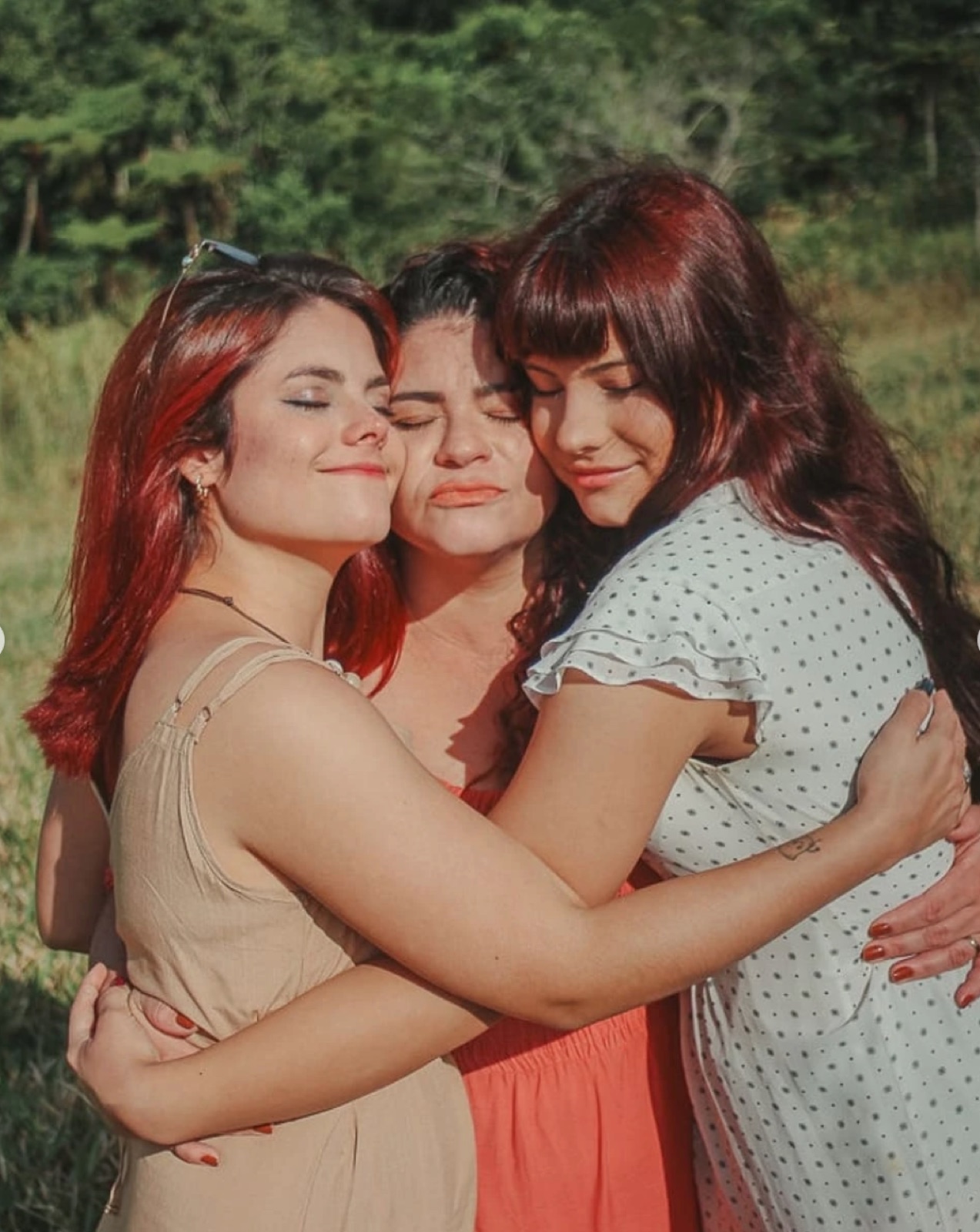 Três mulheres da família se abraçando ao ar livre