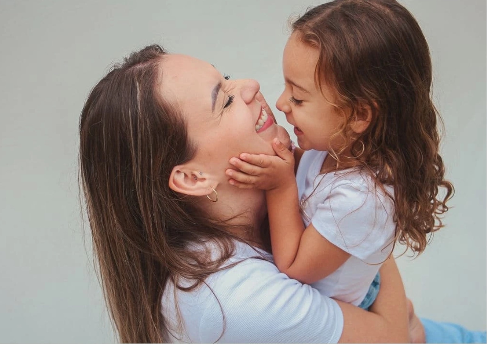 Mãe e filha se tocando o rosto, sorrindo
