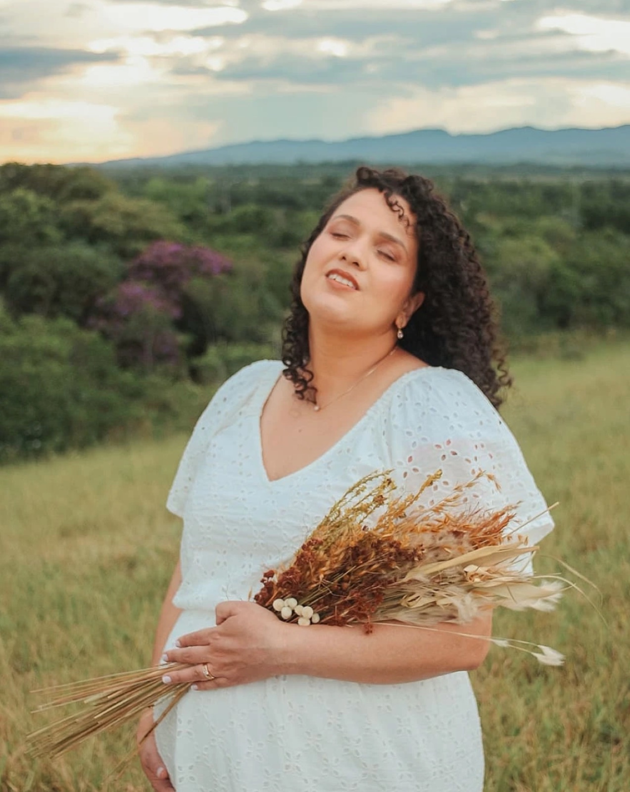 Gestante em vestido branco segurando flores secas no campo