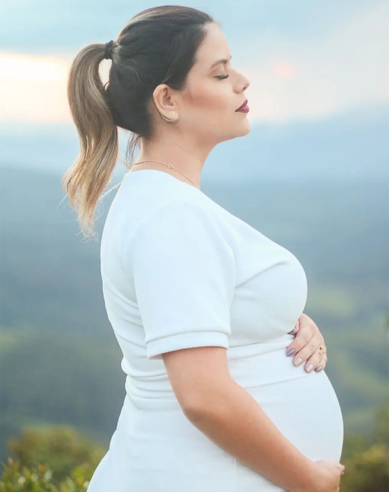 Perfil de gestante em vestido branco na montanha