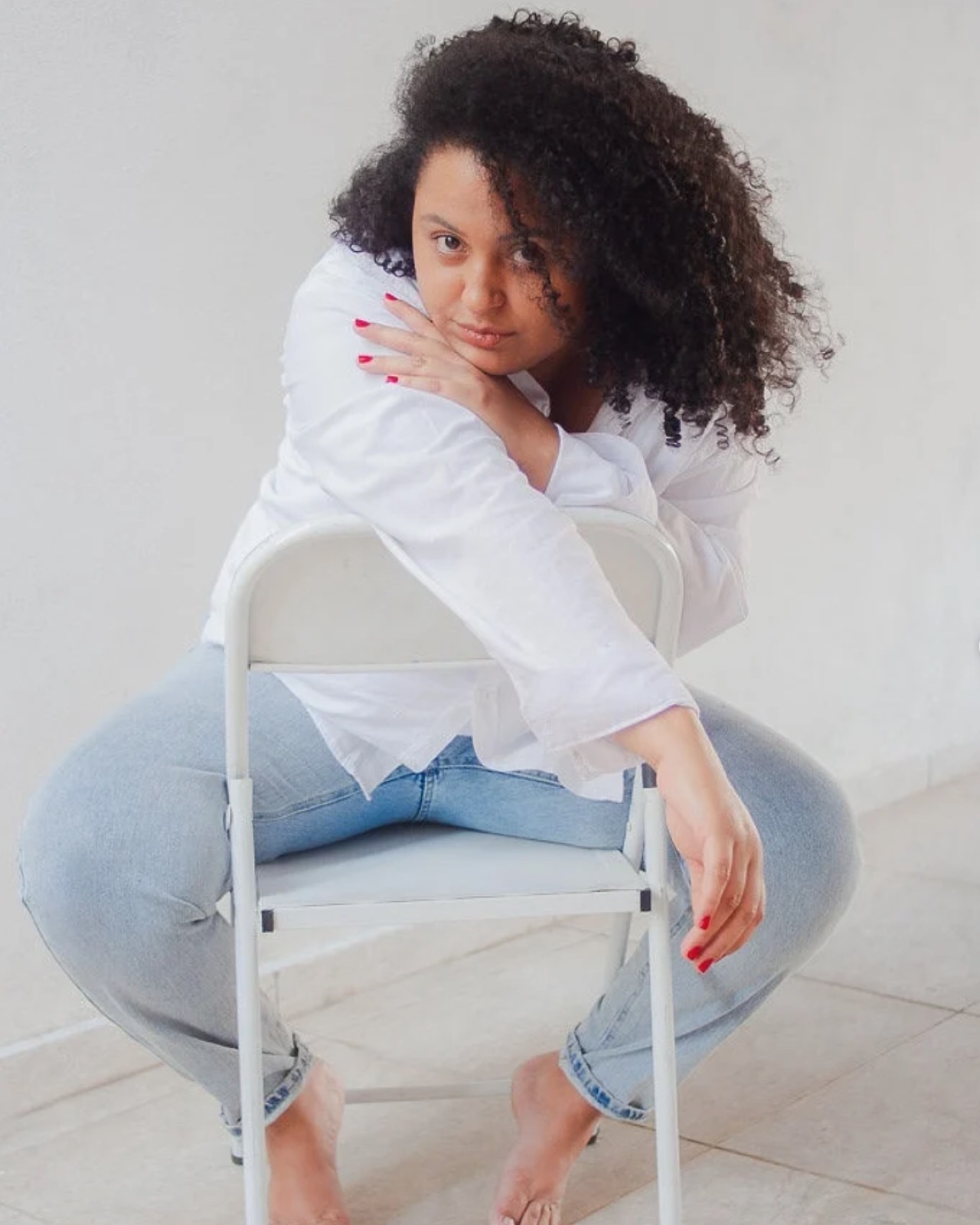 Mulher de cabelo cacheado apoiada em cadeira